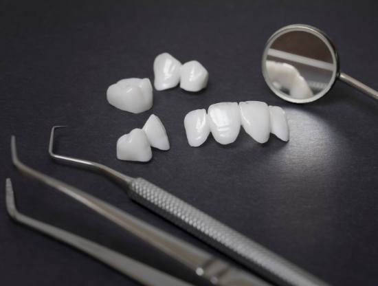Several white dental crowns and veneers on tray next to dental mirrors