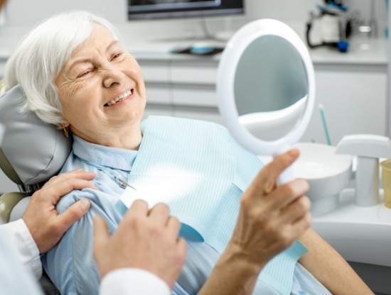 Senior dental patient looking at her smile in a mirror