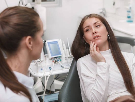 Woman holding her cheek in pain while talking to emergency dentist in Rocky Hill