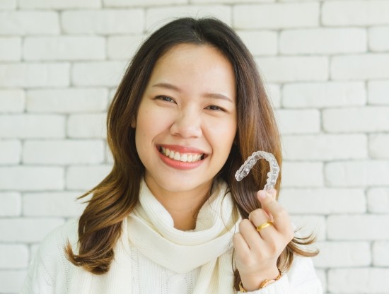 Woman in white sweater smiling and holding a Sure Smile clear aligner