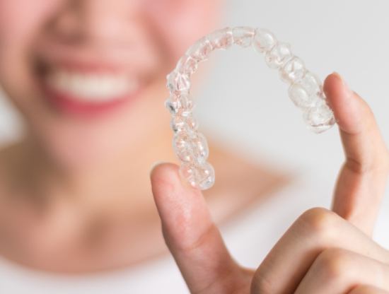 Smiling person holding a clear aligner