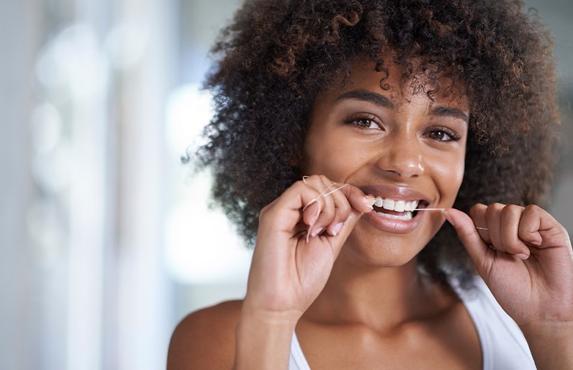 Woman flossing her teeth to maintain healthy smile between preventive dentistry visits