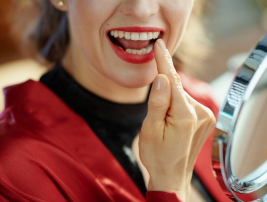 Woman with red lipstick looking at her teeth in mirror