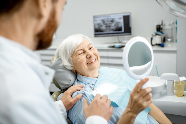 older woman looking at smile in mirror at dentist's office 