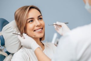 Woman with light brown hair sitting in dental chair smiling at the dentist who is holding cleaning instruments near her mouth