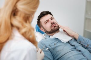 concerned implant patient holding his face in the dentist’s chair